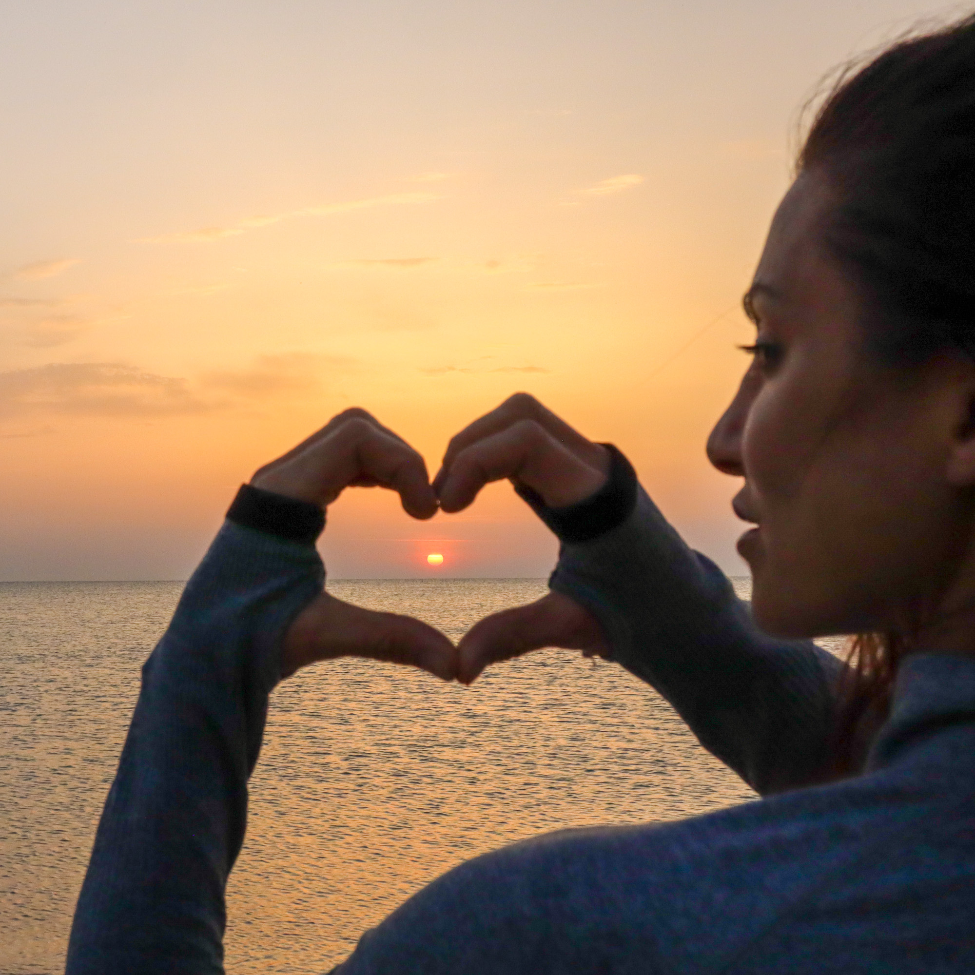 woman alone at dawn on beach with sunrise doing a heart shape around the sun