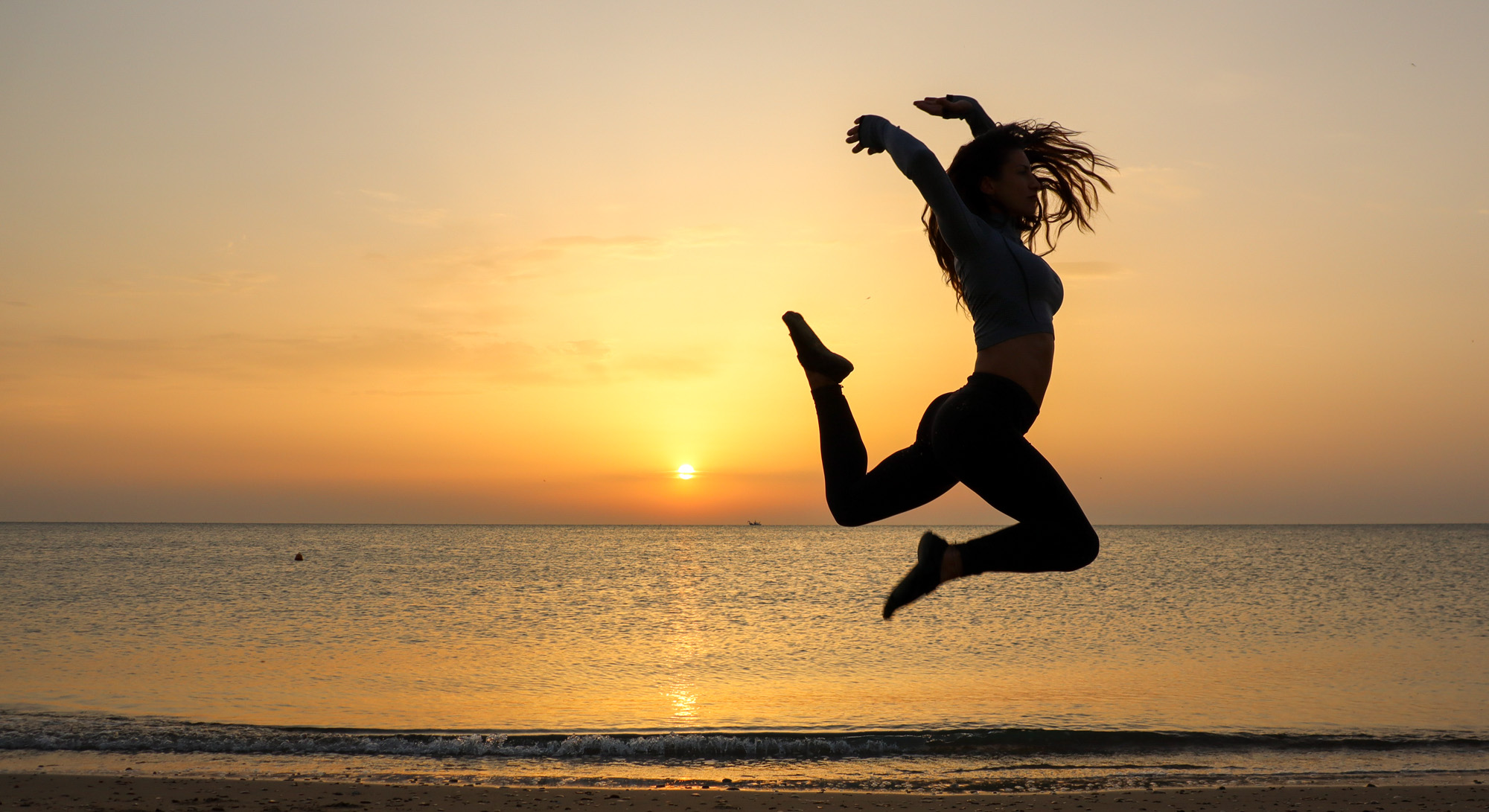 woman alone at dawn on beach with sunrise doing a jump