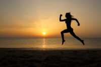 woman alone at dawn on beach with sunrise running